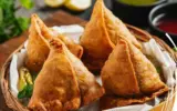 Golden brown, perfectly crimped halwai-style samosas stacked on a platter, ready to be served.