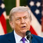 Donald Trump speaking at a rally, with a backdrop suggesting international relations.