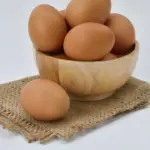 A person holding a carton of eggs with a question mark graphic overlayed, symbolizing the question of how many eggs per day are safe.