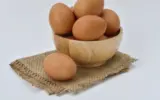 A person holding a carton of eggs with a question mark graphic overlayed, symbolizing the question of how many eggs per day are safe.