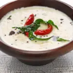 Close-up of a bowl of coconut chutney with a spoon, highlighting its texture and ingredients.