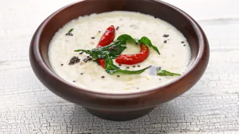 Close-up of a bowl of coconut chutney with a spoon, highlighting its texture and ingredients.