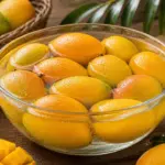 A basket of ripe, yellow mangoes on a wooden table, ready to be enjoyed.