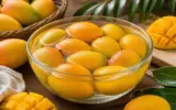 A basket of ripe, yellow mangoes on a wooden table, ready to be enjoyed.