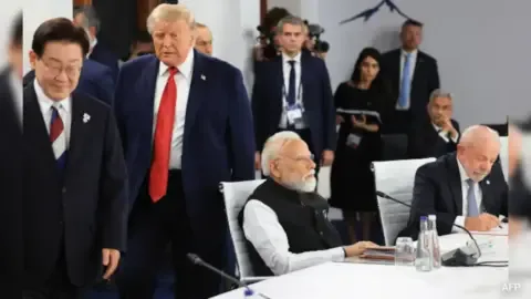 Donald Trump at the G7 Summit, smiling and gesturing.