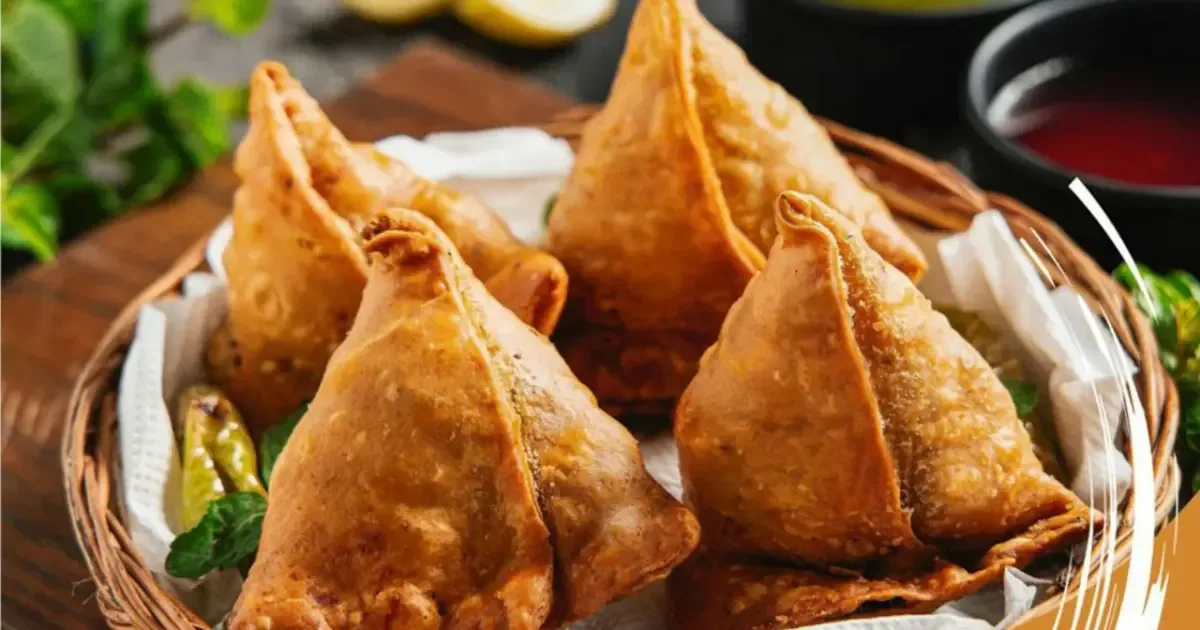 Golden brown, perfectly crimped halwai-style samosas stacked on a platter, ready to be served.