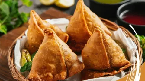 Golden brown, perfectly crimped halwai-style samosas stacked on a platter, ready to be served.