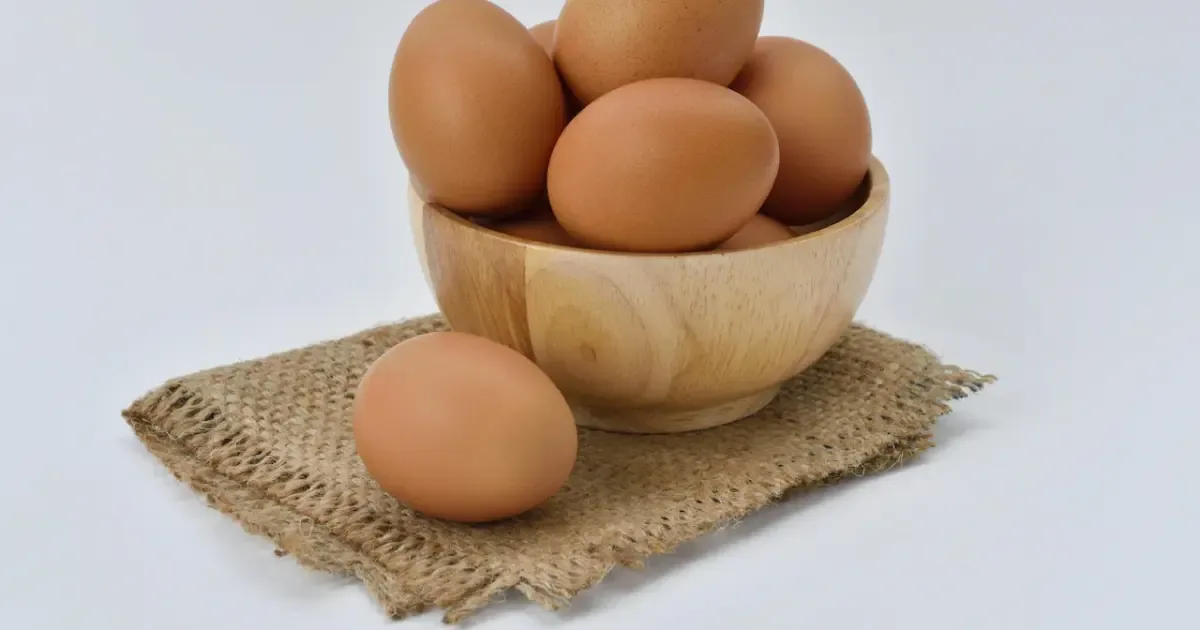 A person holding a carton of eggs with a question mark graphic overlayed, symbolizing the question of how many eggs per day are safe.