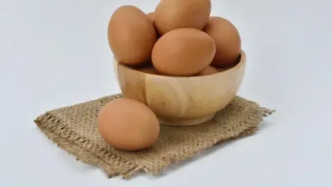 A person holding a carton of eggs with a question mark graphic overlayed, symbolizing the question of how many eggs per day are safe.