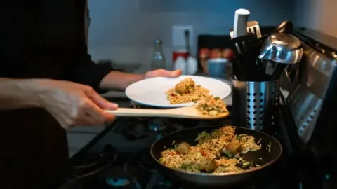 Person carefully reheating food in a microwave, illustrating safe reheating practices for leftovers.